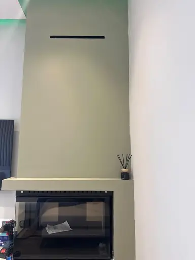 A black reed diffuser placed on the shelf of an olive-toned fireplace.
