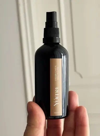 A hand holding the YUMA Fresh Linen black bottle with a beige label and black spray nozzle.