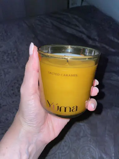 A hand holding the YUMA Salted Caramel scented candle in a glass jar with yellow wax.