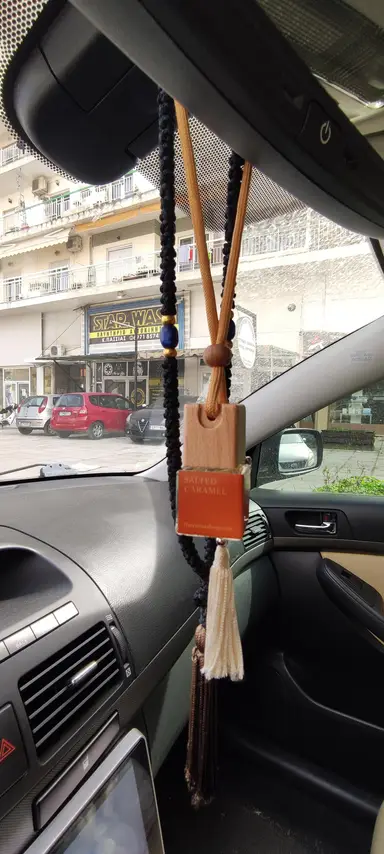 Salted Caramel car diffuser with a wooden cap hanging from a mirror next to a decorative worry bead strand.