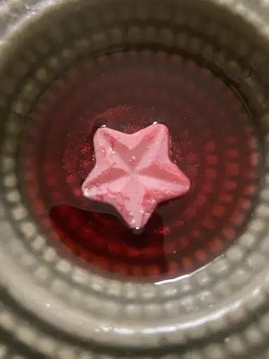 A pink star-shaped wax melt dissolving in red liquid wax on top of a wax warmer.