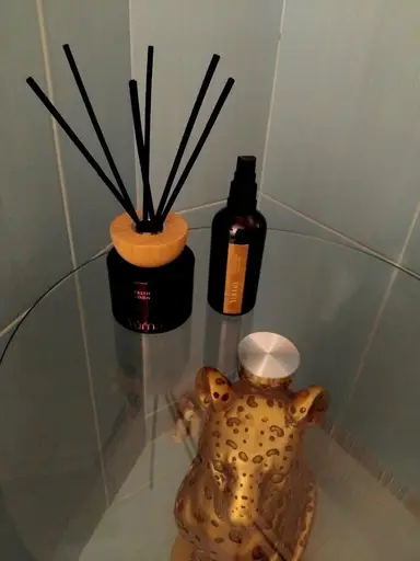 A reed diffuser with black sticks, a room fragrance spray, and a gold leopard ornament on a glass table.