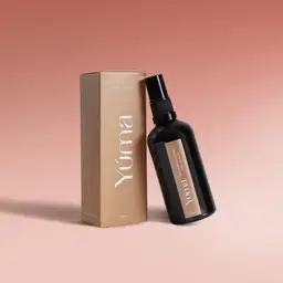 YUMA Melomakarono Fabric Mist in a dark glass bottle beside its paper box on a pink background.