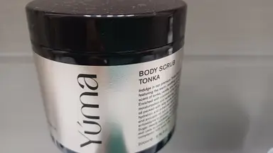 YUMA Body Scrub TONKA dark jar with a silver label and black lid, on a grey background.