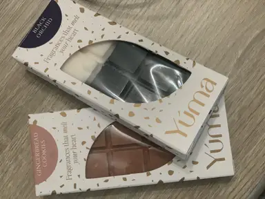 Two YUMA wax melt packages in Black Orchid and Gingerbread Cookies scents on a wooden surface.
