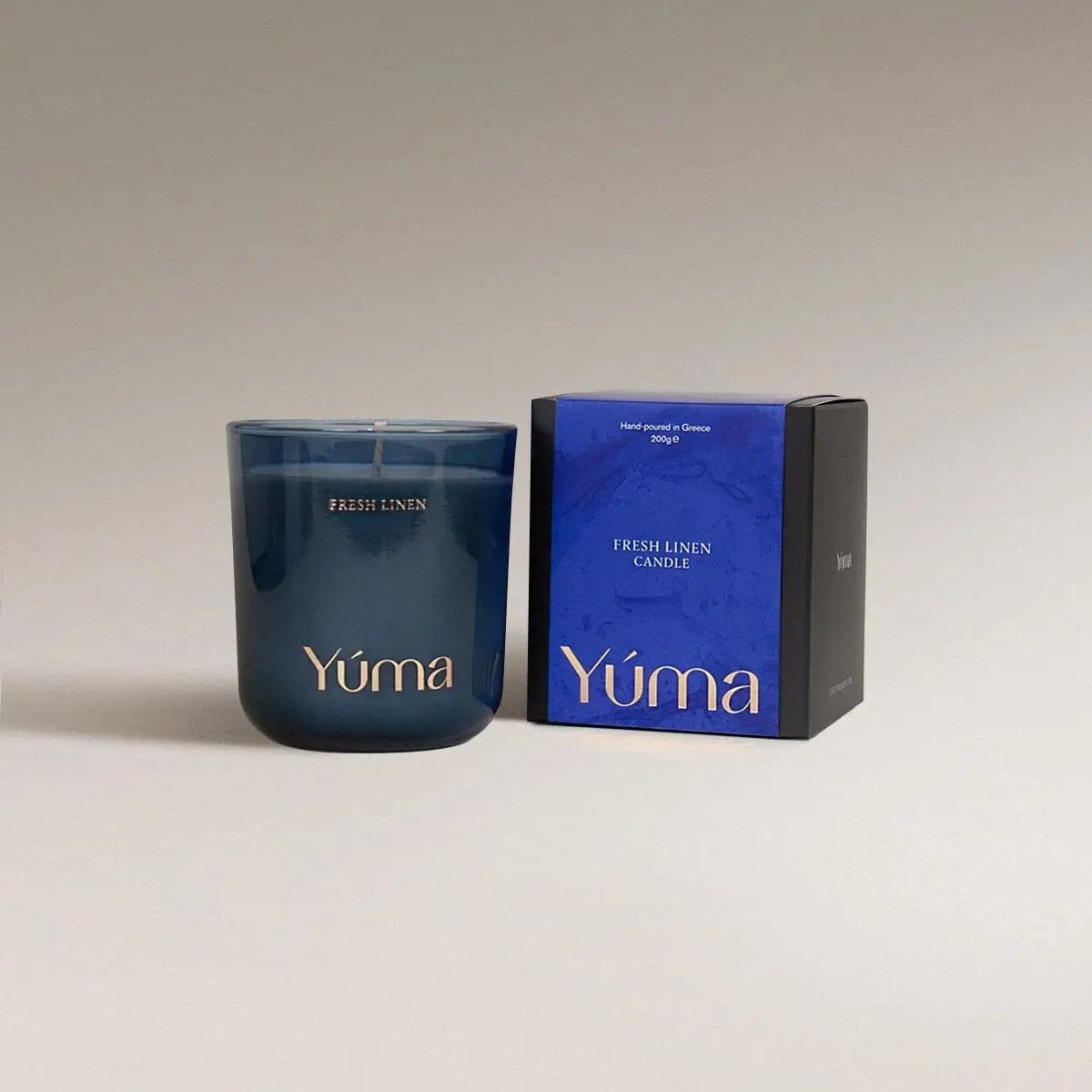 YUMA Fresh Linen scented candle in a blue glass jar next to its paper packaging.