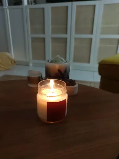 A lit YUMA scented candle in a glass jar on a wooden table with a blurred background.