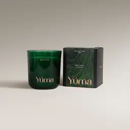 YUMA Pine Tree candle in a green glass vessel beside its paper packaging on a grey background.