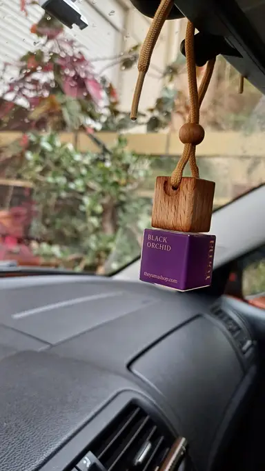 YUMA Black Orchid car fragrance in purple glass with a wooden cap hanging from a car rearview mirror.