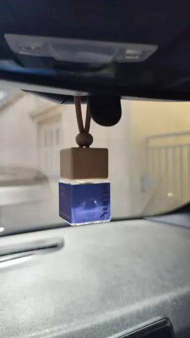YUMA Fresh Linen car fragrance with a wooden cap hanging from a car's interior mirror.