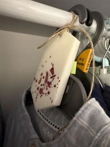 White wardrobe sachet with dried rose petals, hung by twine from a clothes rail.