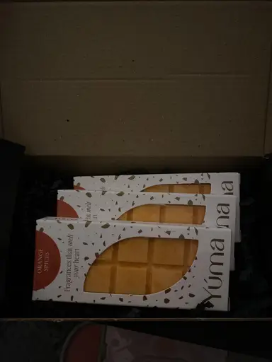 Three YUMA Orange Spices wax melt packages arranged inside a box with black protective paper.