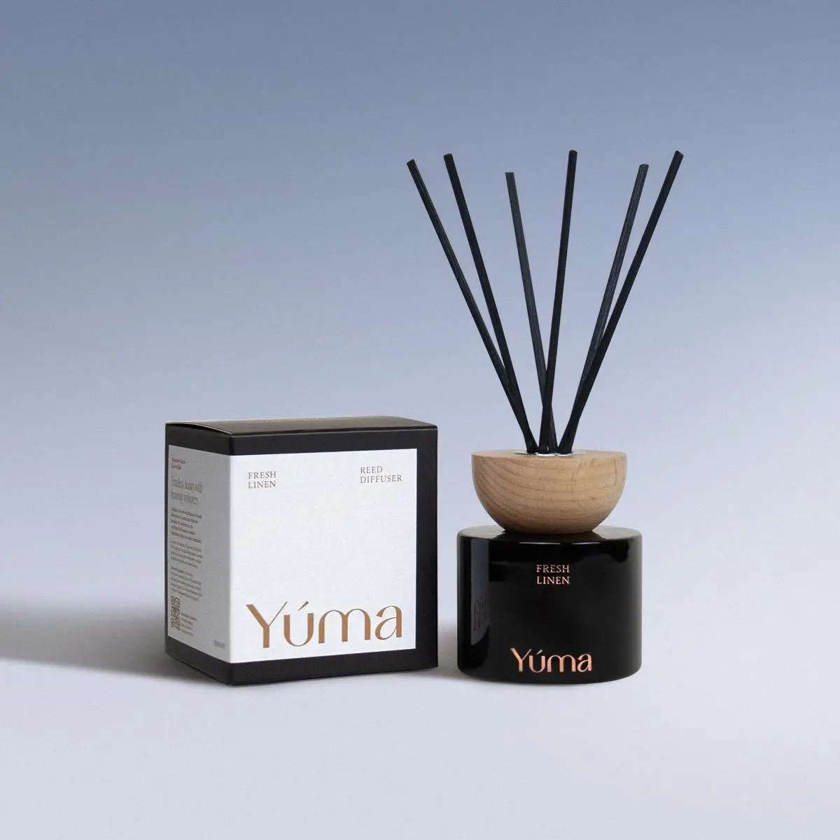 YUMA Fresh Linen reed diffuser in a black glass bottle with a wooden cap, next to its paper packaging.