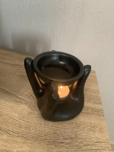 Black ceramic hand-shaped wax burner with a lit tealight and wax melt in the upper dish.