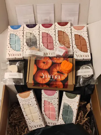 An assortment of YUMA wax melts in various colours and packaging styles inside a paper box.