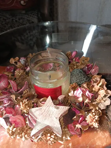 A glass jar candle surrounded by dried flower petals and a wooden decorative star.