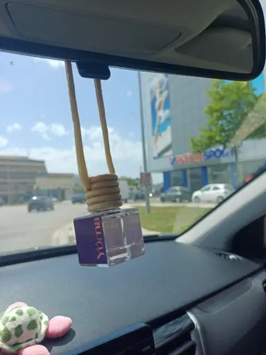 A YUMA car air freshener hanging from a vehicle's rear-view mirror with a road view in the background.