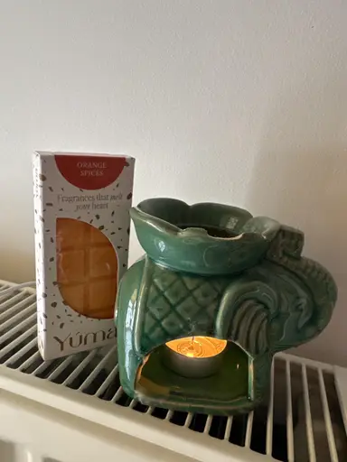 A green ceramic elephant-shaped wax burner with a lit tea light beside a pack of YUMA wax melts.