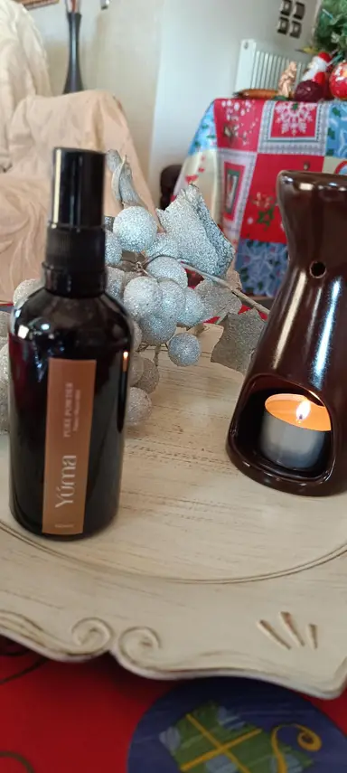 A dark bottle of YUMA Pure Powder room spray next to a wax melt burner with a lit tea light.