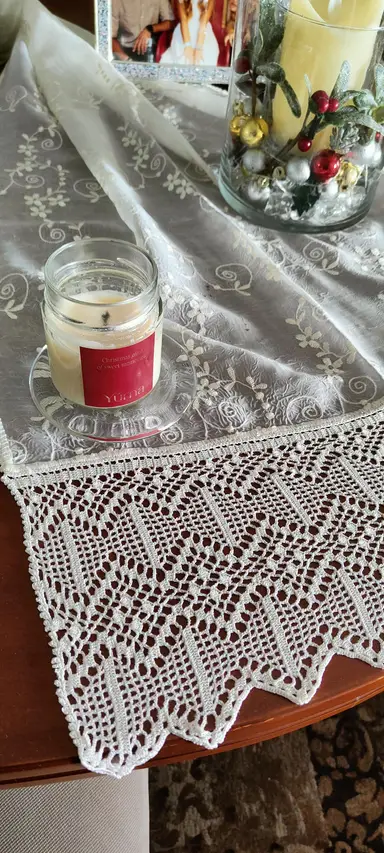 A YUMA scented candle in a glass jar, placed on a white lace tablecloth with Christmas decorations.
