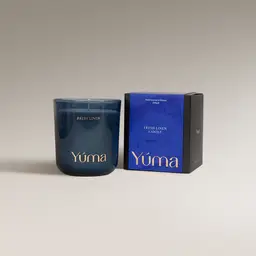 YUMA Fresh Linen candle in a blue glass vessel beside its paper packaging.