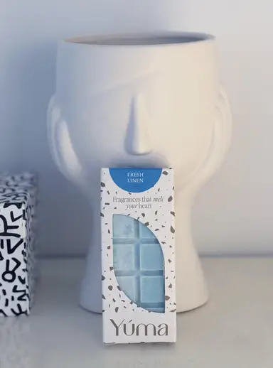 YUMA Fresh Linen wax melt packaging in front of a white ceramic face-shaped vase.