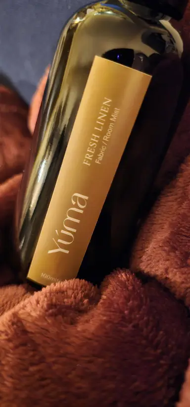 YUMA Fresh Linen dark glass bottle placed on soft brown fabric.