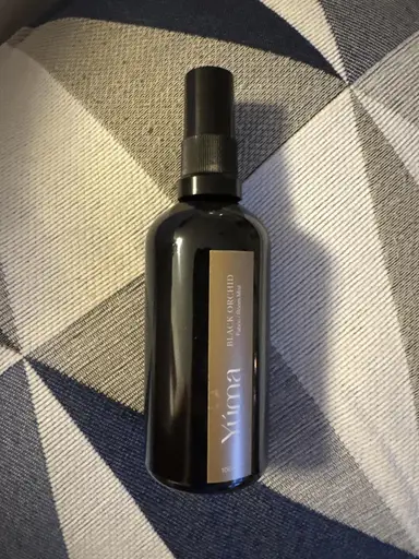 YUMA Black Orchid room spray in a black bottle, placed on fabric with a geometric pattern.
