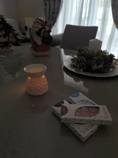 Three YUMA wax melt packages beside a lit white wax warmer and Christmas decorations.