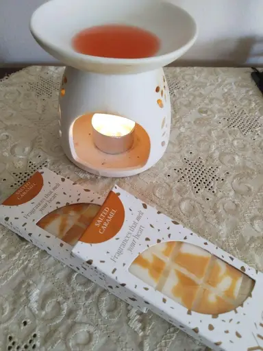 White ceramic wax burner with a lit tealight and melted wax, next to Salted Caramel wax melt packaging.