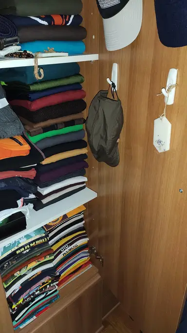 A scented wardrobe sachet hanging on a wooden surface next to stacks of colourful folded clothes.