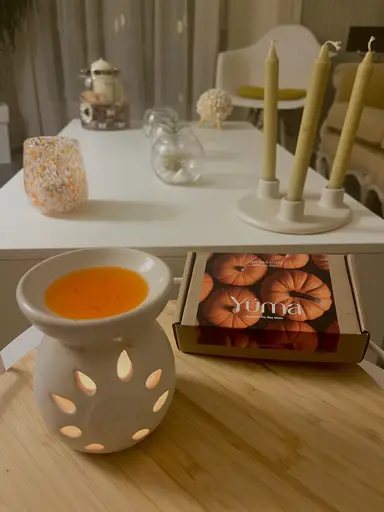 White ceramic oil burner with melted orange wax next to a YUMA Pumpkin Pie Wax Melts box.