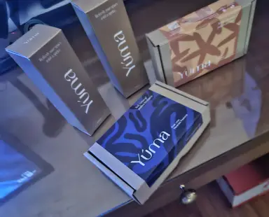 Four YUMA paper gift boxes in various shapes and colors on a glass surface.