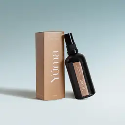 A dark glass YUMA Cycladic Roots spray bottle next to its beige paper packaging.