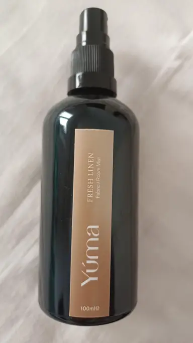 Dark glass YUMA Room Mist bottle with a beige Fresh Linen label, placed on white fabric.