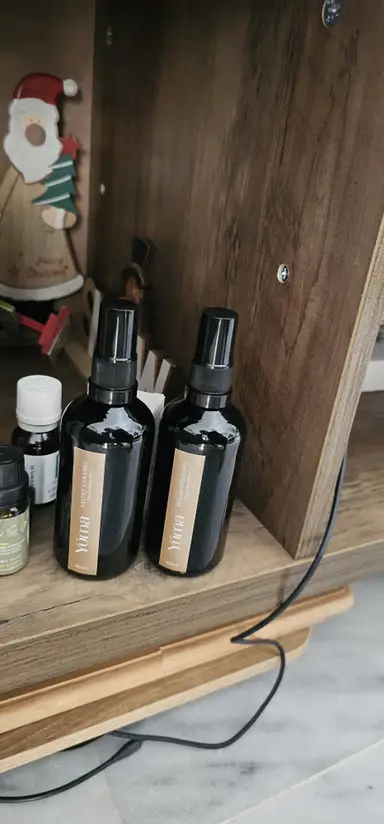 Two black YUMA room spray bottles on a wooden shelf next to Christmas decorations.