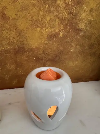 White ceramic burner with a lit candle inside and an orange wax melt melting on top.