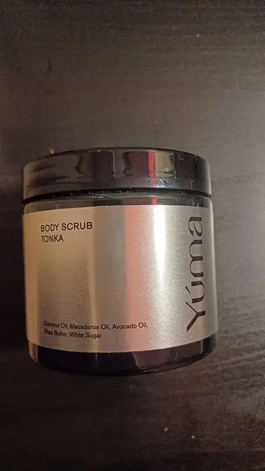 A YUMA Tonka Body Scrub in a black jar with a silver label against a dark background.