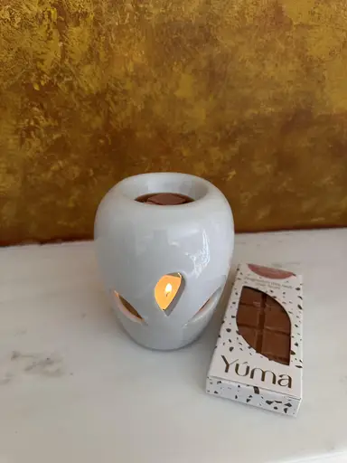 White ceramic burner with a lit tealight beside a YUMA wax melt package on a marble surface.