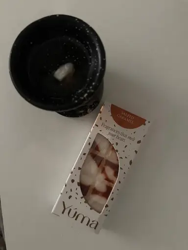 Black wax warmer with melted wax next to a package of YUMA Salted Caramel wax melts.