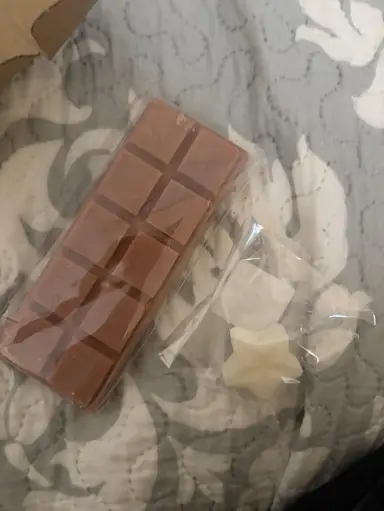 A brown chocolate-shaped bar of wax and two small white candles in clear packaging.
