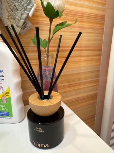 Black YUMA Pure Powder reed diffuser with a wooden cap and black reeds on a white surface.