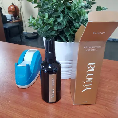 A dark YUMA room spray bottle next to its packaging and a blue piece of tape.