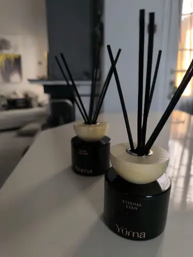 Two black YUMA reed diffusers with wooden caps and black reeds on a white surface.