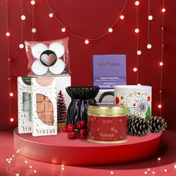 YUMA Christmas Gift Set with wax melts, a scented candle, a mug, and decorative pine cones on a red background.