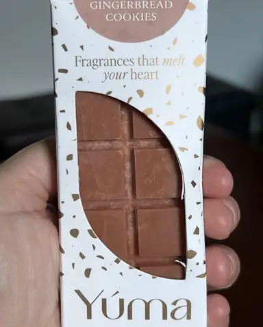 A hand holding YUMA's white packaging for chocolate-shaped Gingerbread Cookies wax melts.