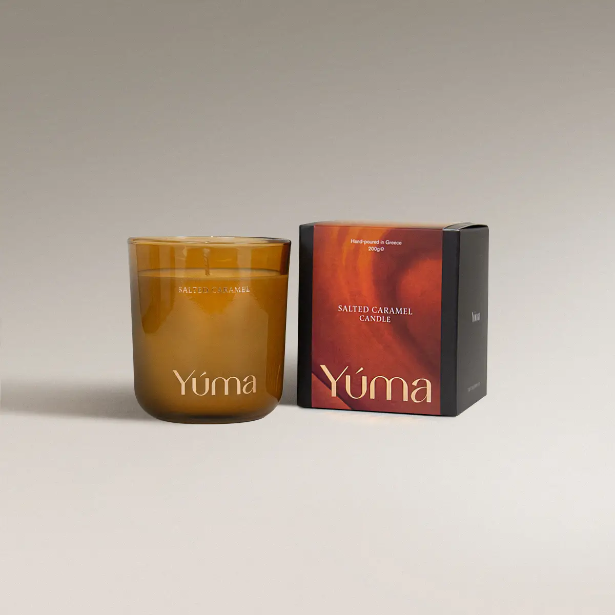 YUMA Salted Caramel candle in an amber glass vessel beside its paper packaging.