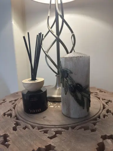 YUMA Salted Caramel reed diffuser and a decorative candle with an olive branch design on a wooden table.
