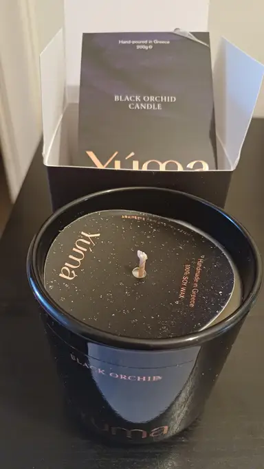YUMA Black Orchid candle in a black glass jar, displayed in front of its open packaging.