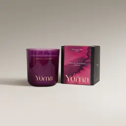 YUMA Apple Cinnamon candle in a smoky pink glass vessel beside its paper packaging.
